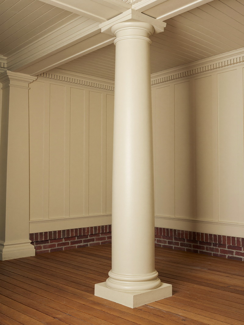 A restored porch corner on a historic Lexington colonial: one crisp ivory round column on warm cedar decking, ivory beadboard ceiling above