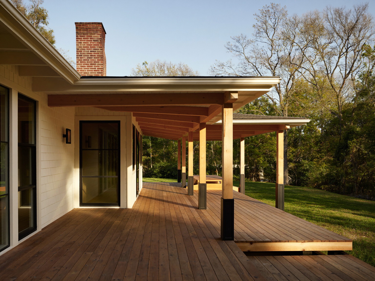 A completed covered cedar deck off a historic Lexington home at golden hour: warm oiled boards, slender posts, a red-brick chimney above the low roofline