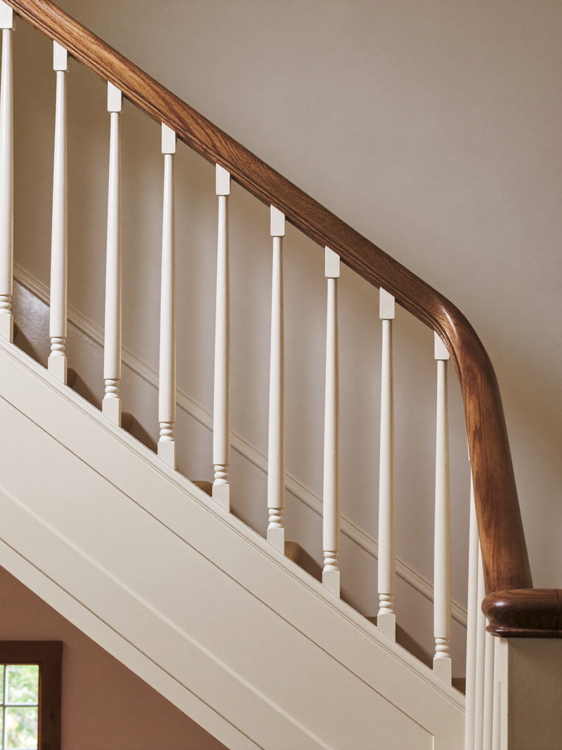 A repaired stair balustrade in a historic colonial stairwell: one new crisp ivory baluster fitted among originals beneath a refinished dark-stained handrail