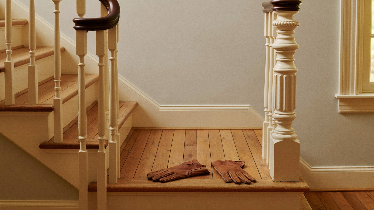 A quiet work moment in the front hall of a historic Lexington Massachusetts colonial: completely plain bare tan leather work gloves resting on the maple bottom stair trea