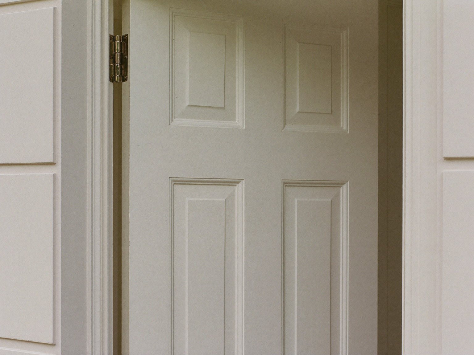 A traditional ivory painted front door standing slightly open in its freshly serviced frame inside a colonial entry: raised panels visible, smooth refreshed edge