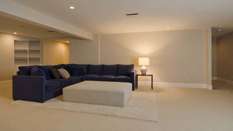 A finished suburban lower-level family room: warm greige walls, white built-in media wall with warm wood console, comfortable navy sectional