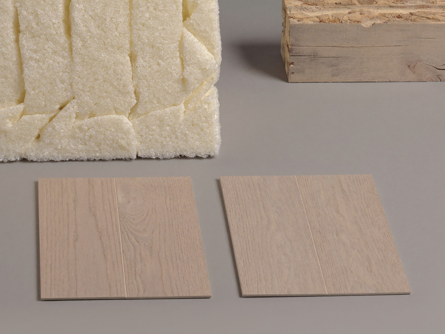 Still life photograph of moisture-smart basement materials: oak-tone vinyl plank samples, rigid foam insulation corner, treated lumber offcuts