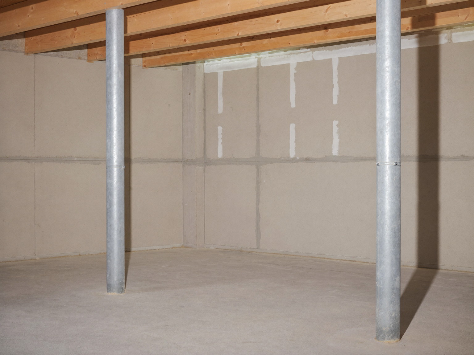 An honest unfinished suburban basement: poured concrete foundation walls, steel support columns, wood joists overhead, bare concrete floor