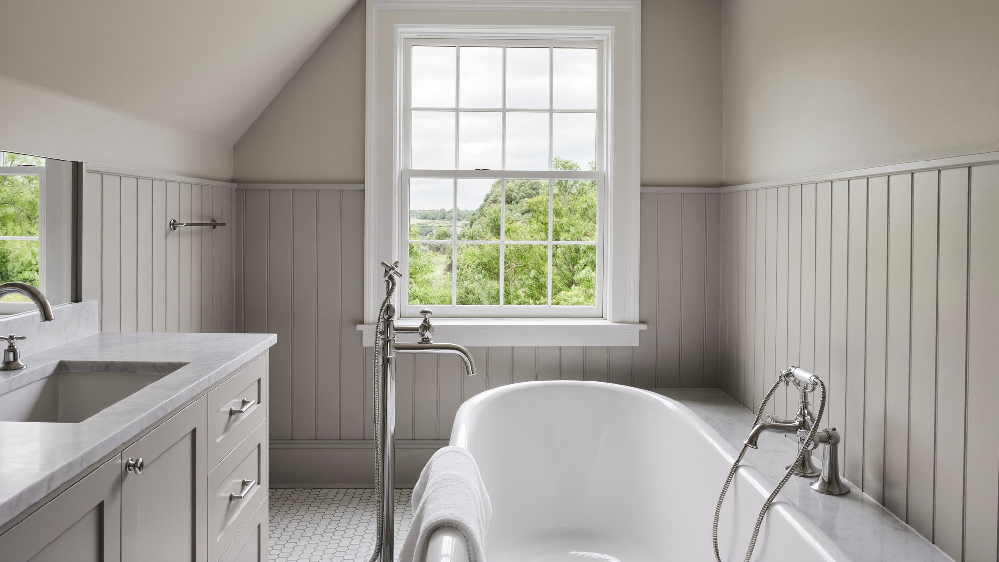 a serene renovated bathroom in a classic Medfield Massachusetts colonial: white double-hung window with traditional trim, freestanding tub