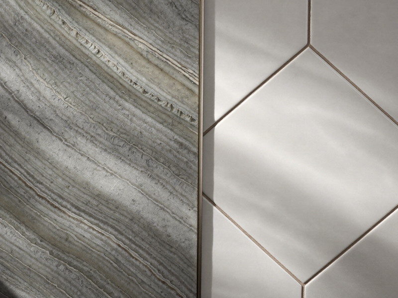 Macro photograph where honed gray-veined marble meets white beveled ceramic tile with a crisp caulk line, slim nickel trim strip between, beautiful raking light