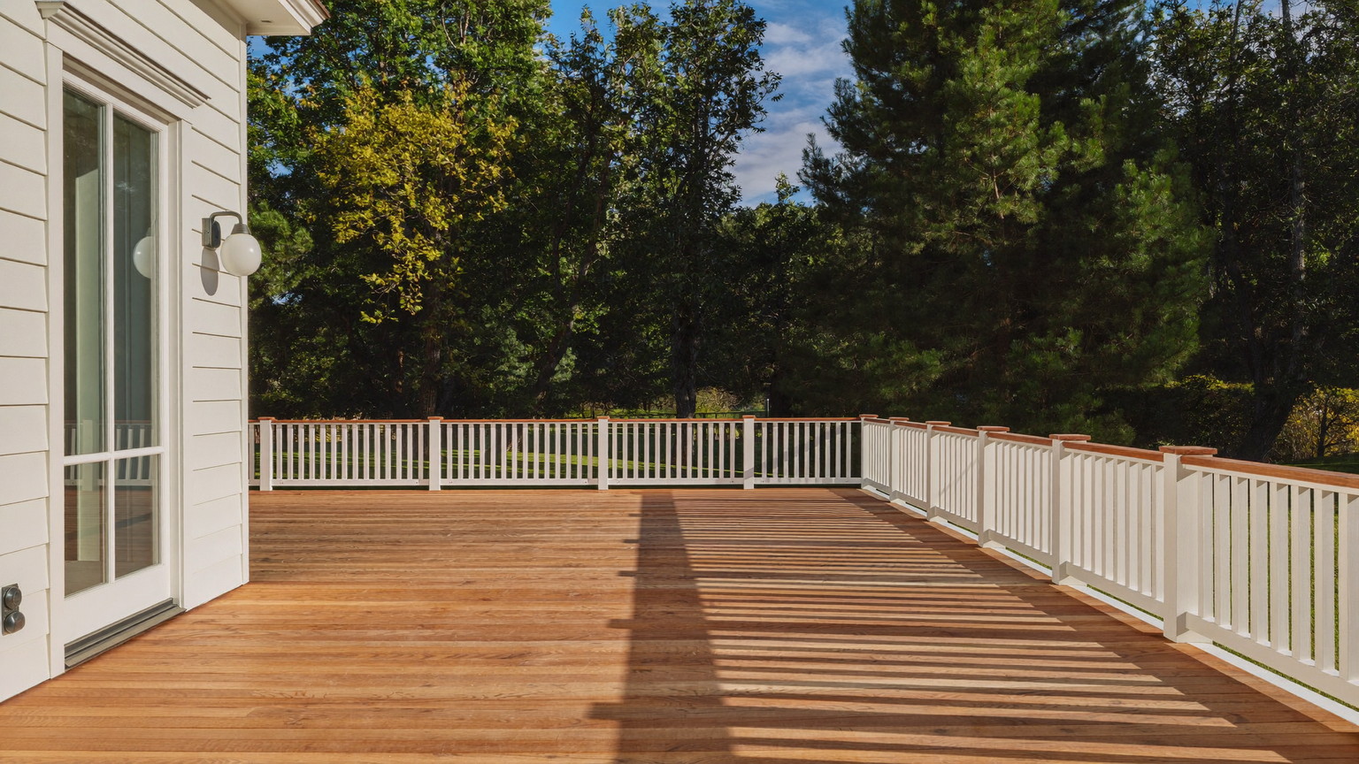 Panoramic editorial photograph of a spacious cedar deck behind a white New England colonial: warm cedar boards freshly finished