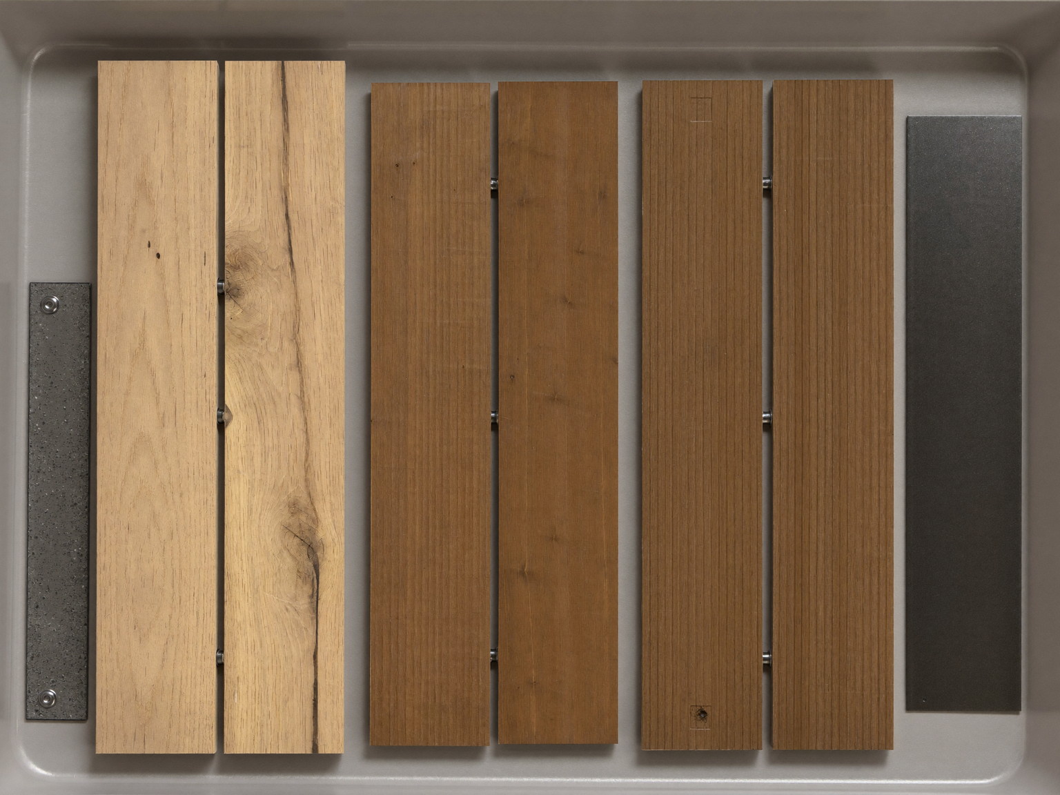 Still life photograph of decking materials arranged on a neutral gray tray: cedar deck board samples and warm brown composite deck board samples laid side by