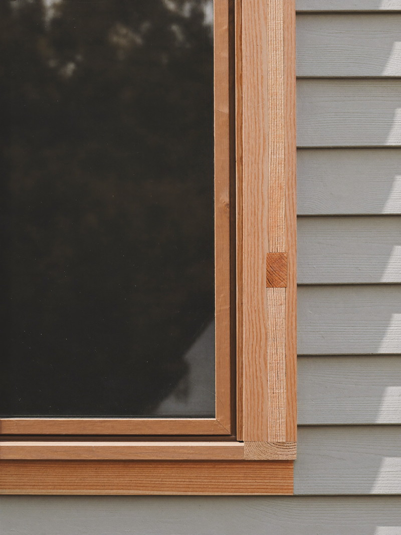 New primed window casing repairs with raw wood dutchman patches fitted against older clapboard siding on a suburban home, tight joinery, honest repair detail