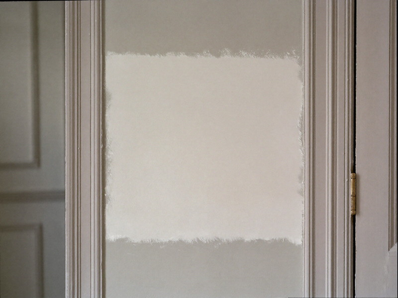 A drywall patch primed and feathered smooth beside original door trim in a colonial hallway, ready for paint, clean and orderly