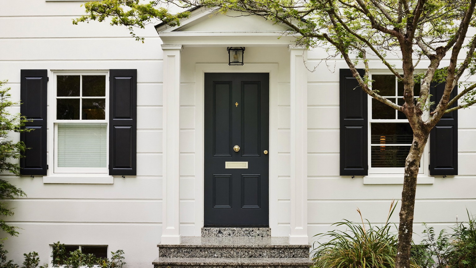 A beautifully kept white New England colonial facade: clean granite front step, freshly painted deep charcoal door with plain unmarked surface