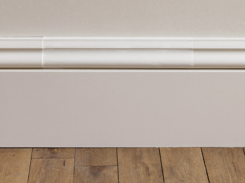 Repaired baseboard trim joined tight to the original millwork, primed and painted to match, oak flooring below