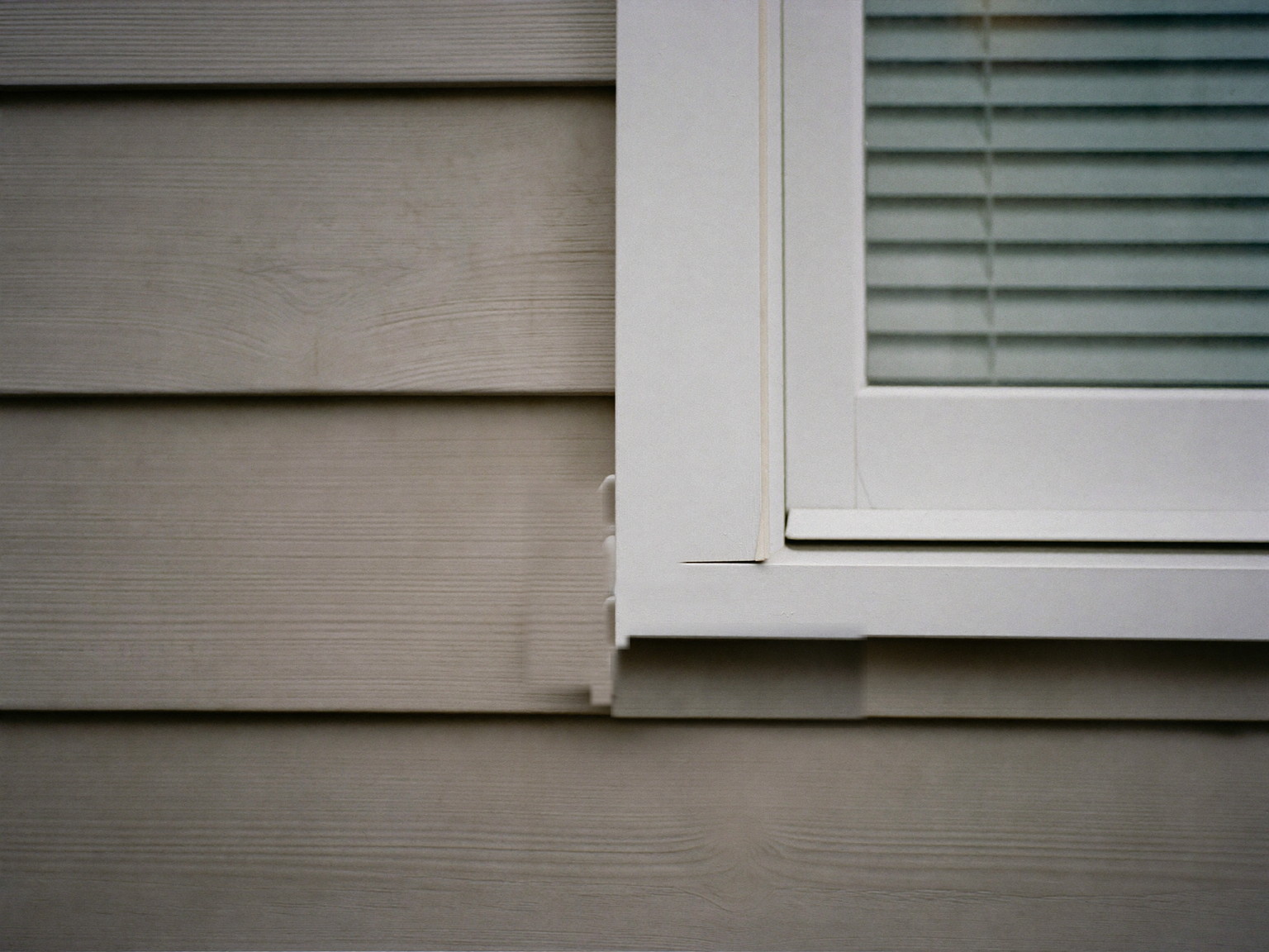 A fresh white weatherproof sealant line along the joint where clapboard siding meets a white painted window casing on a New England home
