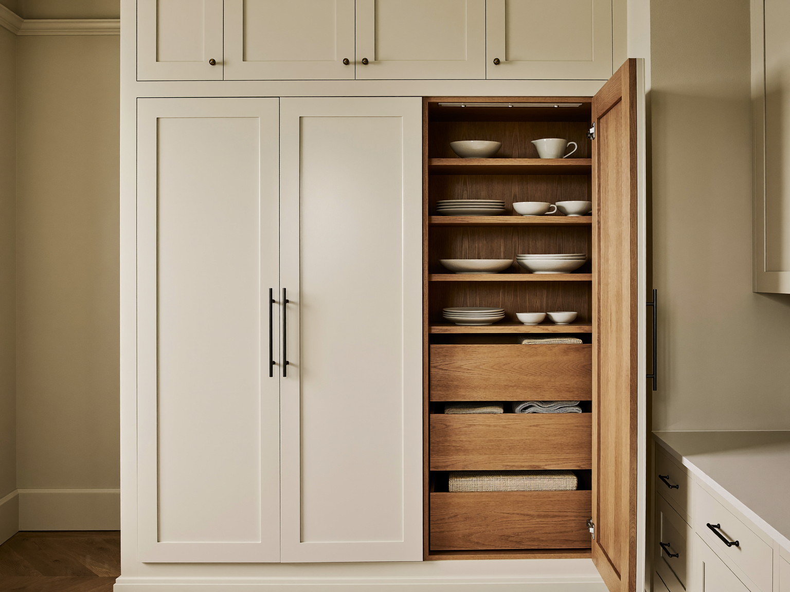 Custom floor-to-ceiling pantry joinery in a suburban colonial kitchen: tall cream cabinets open to oak-faced drawers and shelves holding plain white ironston