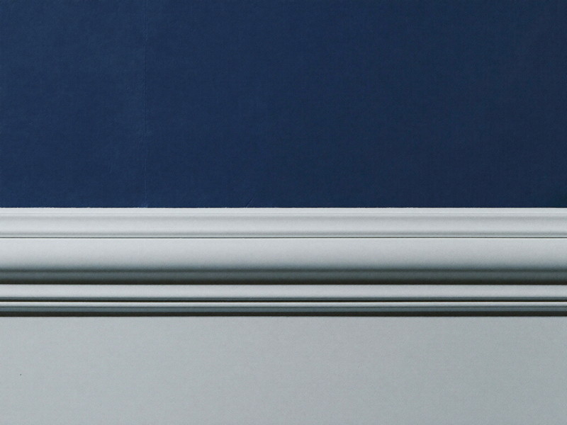 Close-up of a crisp hand-cut paint line where a deep navy wall meets bright white painted trim, razor-straight edge, raking light