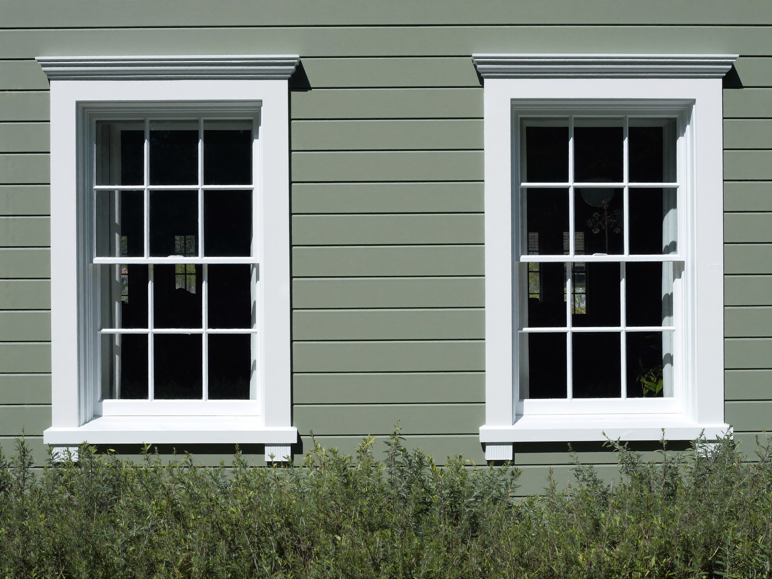 A New England colonial facade detail after repainting: fresh white window casings and corner boards against muted sage clapboard, crisp shadow lines