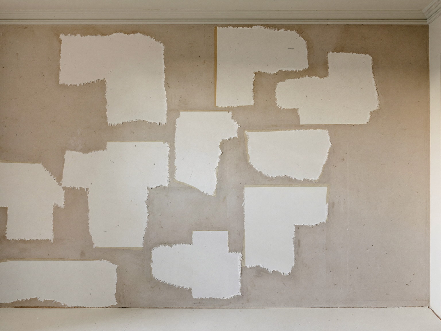 An older plaster wall mid-preparation in a colonial home: sanded joint-compound patches feathered smooth, simple crown molding above