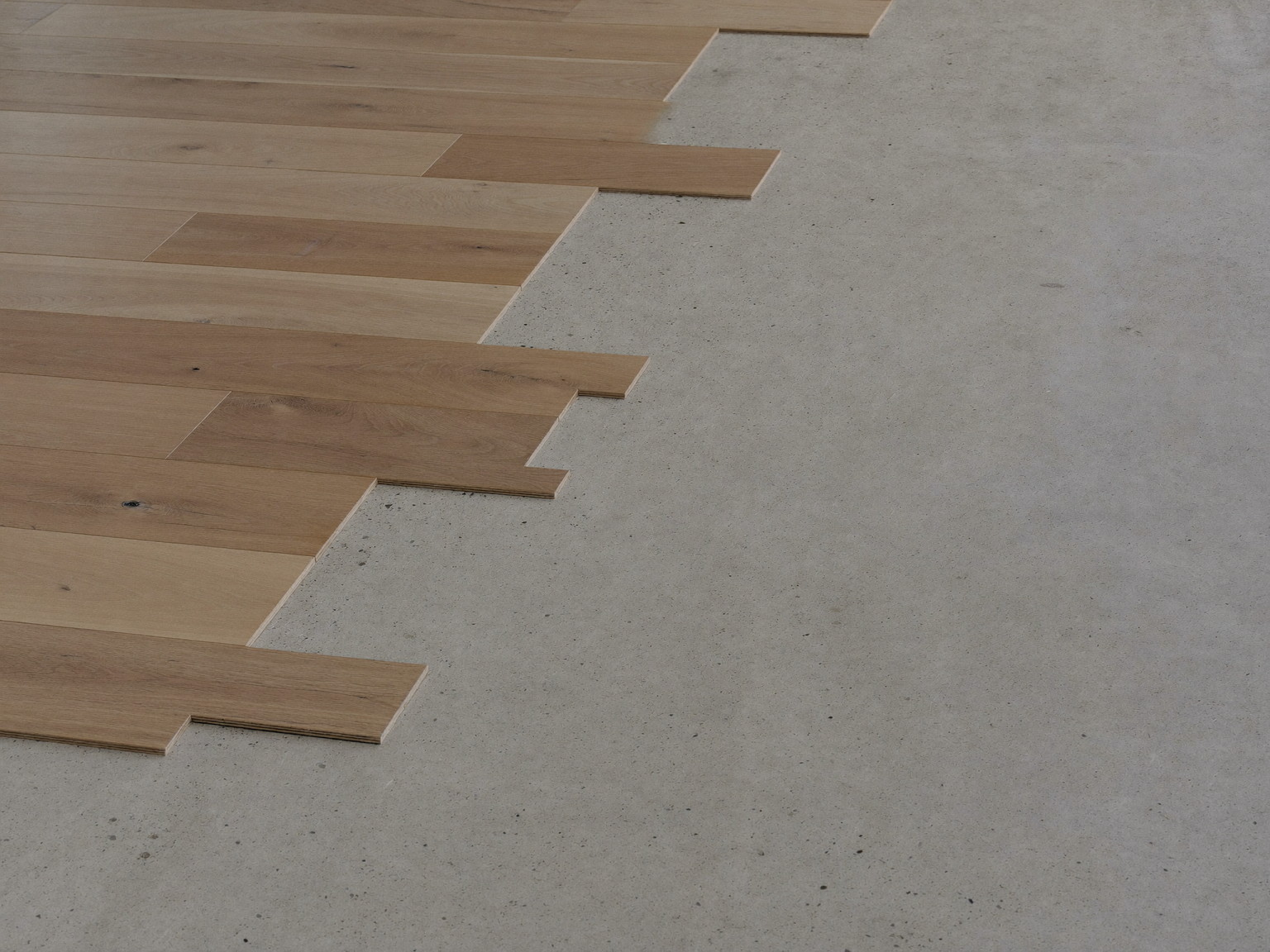 Wide plank flooring mid-installation across a clean swept basement floor, the neat transition line showing smooth bare concrete beside finished planks,