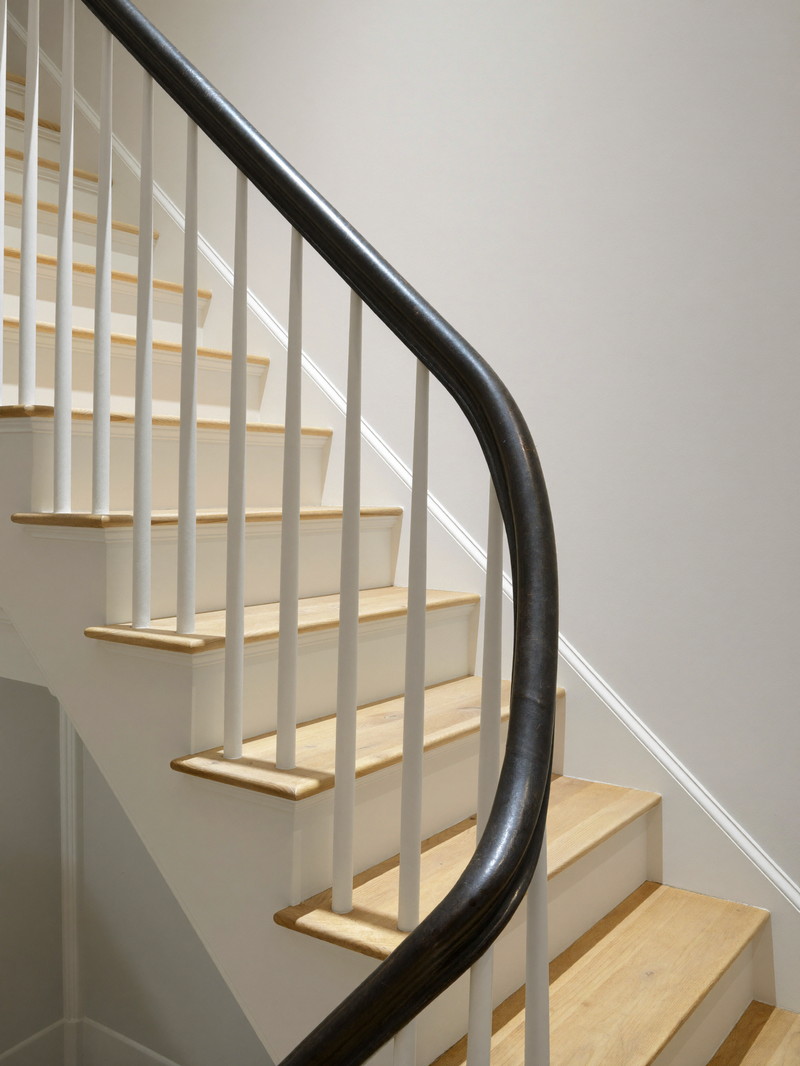 A refinished basement stair in a comfortable colonial: warm white risers and stringers, pale wood treads, a simple round matte black handrail on plain