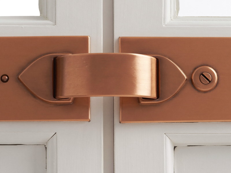 Close view of a traditional brushed copper window sash lock with a curved swing arm where two white painted wooden sashes meet, smooth plain metal, crisp