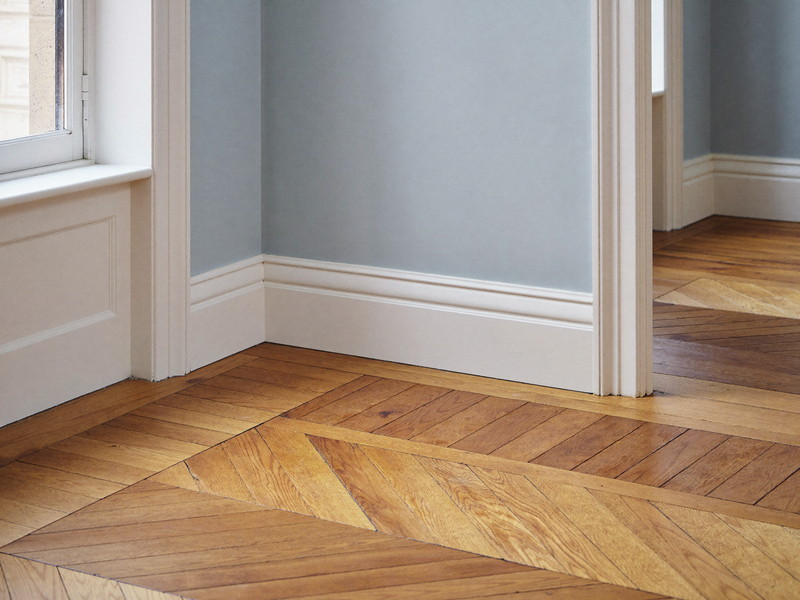 A restored corner where crisp white painted baseboard and door casing meet a refinished golden oak floor in a comfortable colonial room, freshly painted