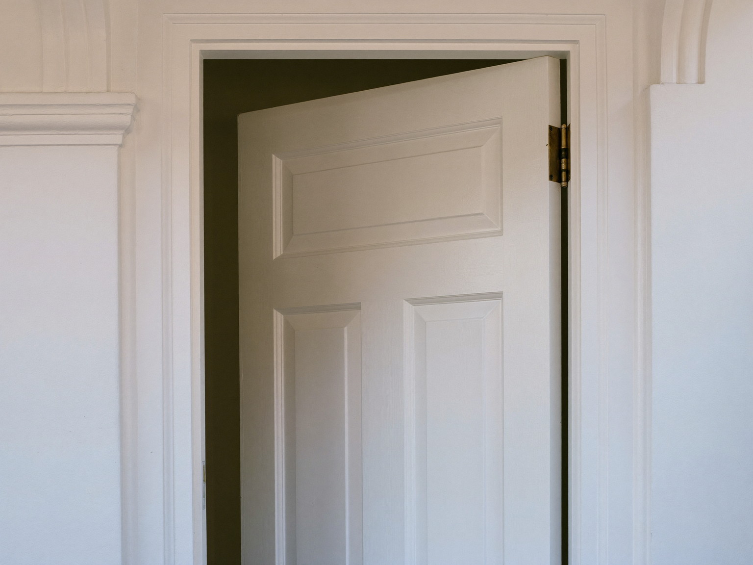 A traditional white painted front door standing slightly open in its freshly serviced frame inside a colonial entry: raised panels visible, smooth