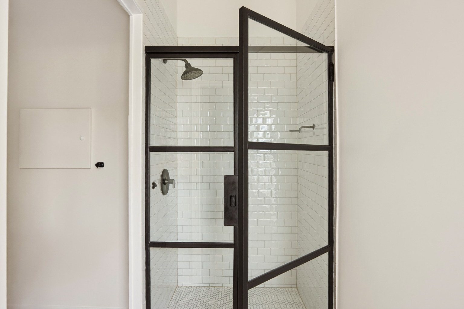 Looking into a bright walk-in shower with a matte black framed glass door in a renovated small-town bathroom: classic white subway tile, matte black