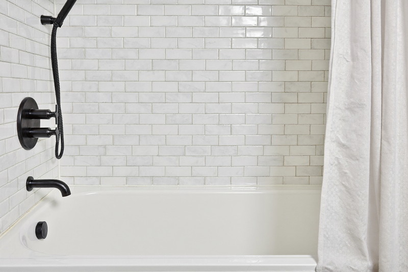 A practical tub and shower combination in a small-town family bathroom: white tub, white subway tile surround, matte black fixtures, simple white shower