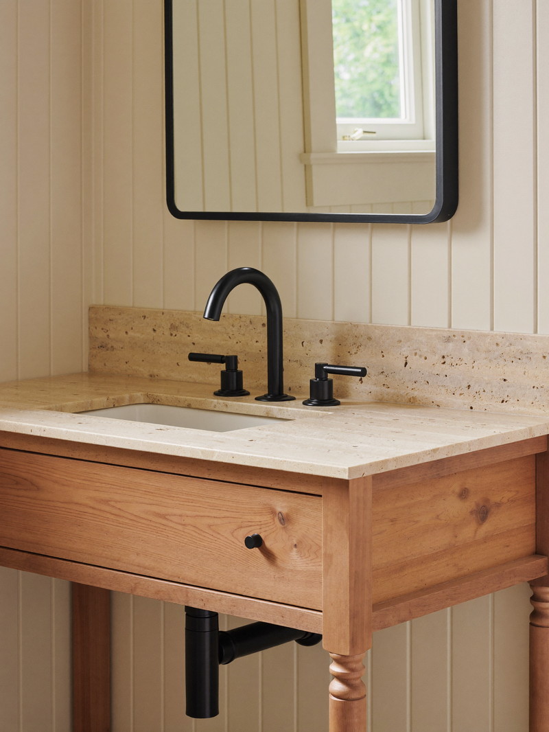 A warm knotty pine bathroom vanity with a creamy stone top and matte black faucet with smooth lever handles, rectangular black-framed mirror on a cream