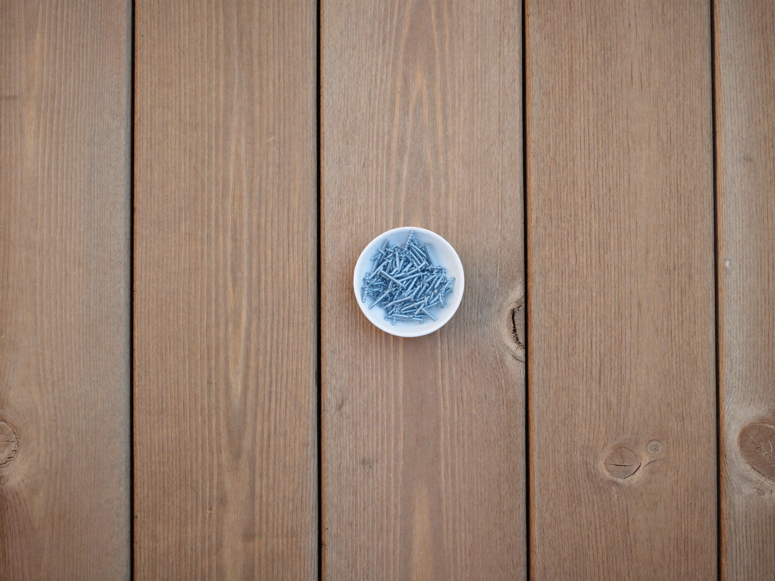 Overhead view of new pressure-treated deck boards with visible natural wood grain laid side by side, a small plain white ceramic dish of straight smooth