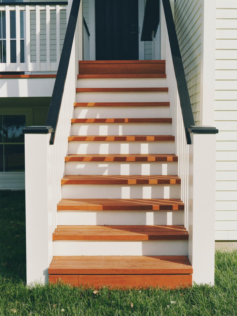 Refreshed wooden deck stairs on a well-kept small-town colonial: warm honey-toned treads, crisp white risers and square balusters, simple matte black