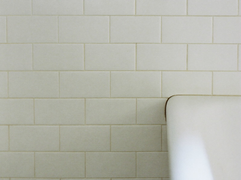 A clean bright white bathtub edge meeting classic white subway wall tile, the joint freshly finished, smooth and tidy, completely bare tub edge, soft