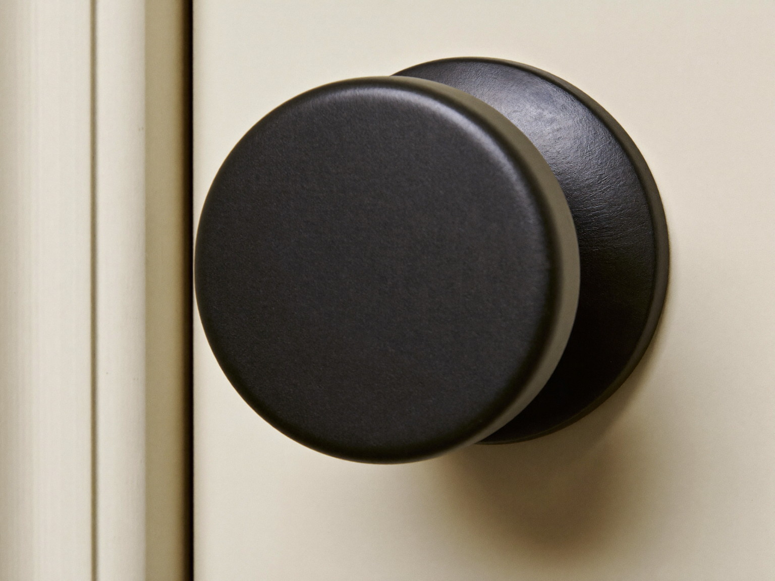 Macro photograph of a matte black round door knob with a perfectly plain smooth face on a simple round rosette, mounted on a cream paneled door, simple