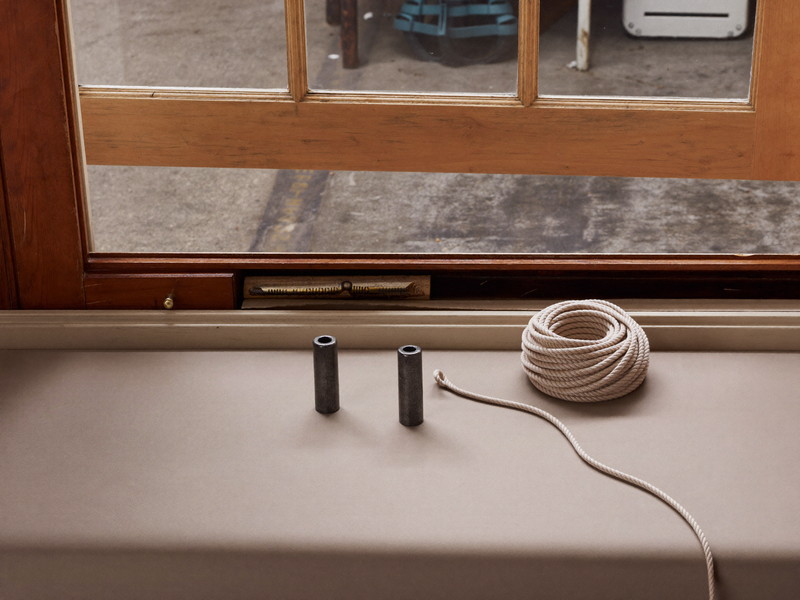 Mid-service on a workshop bench: a colonial double-hung wooden sash tilted open, soft twisted cotton sash cord in a neat coil beside two plain smooth