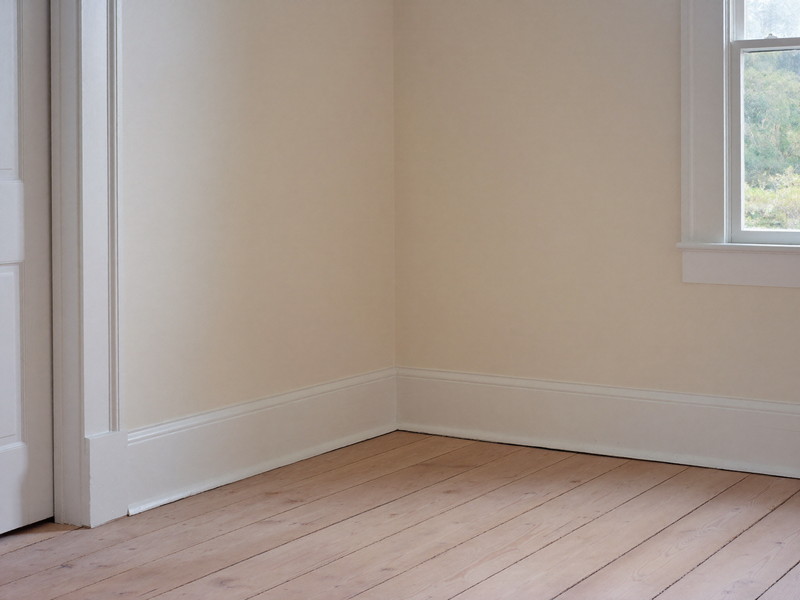 One restored corner of a well-kept colonial room, where crisp white painted baseboard and door casing meet a refinished wide pine floor, freshly painted