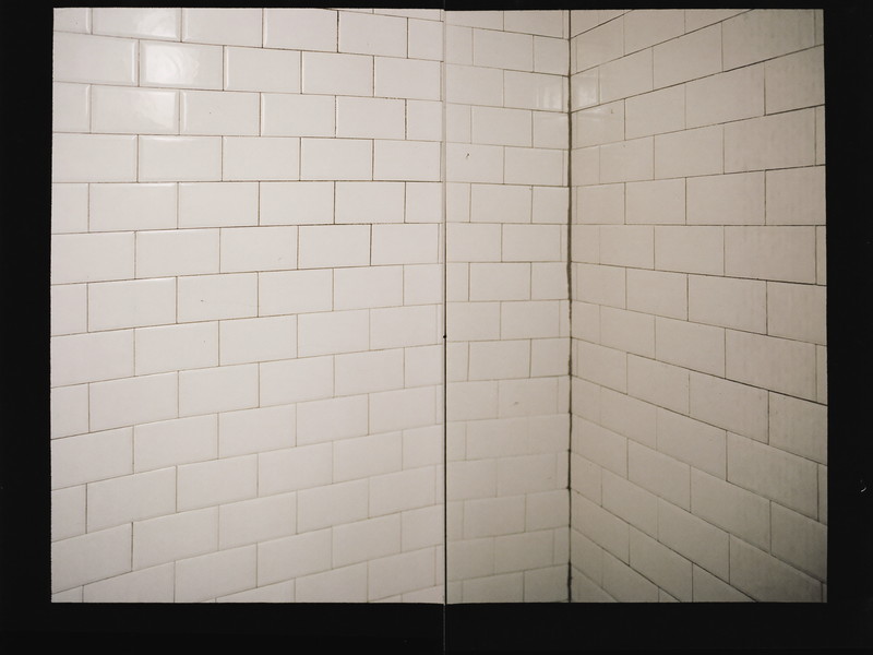 Freshly regrouted classic white subway tile in a small-town shower corner: clean bright grout lines, every tile flat and straight, matte black fitting at
