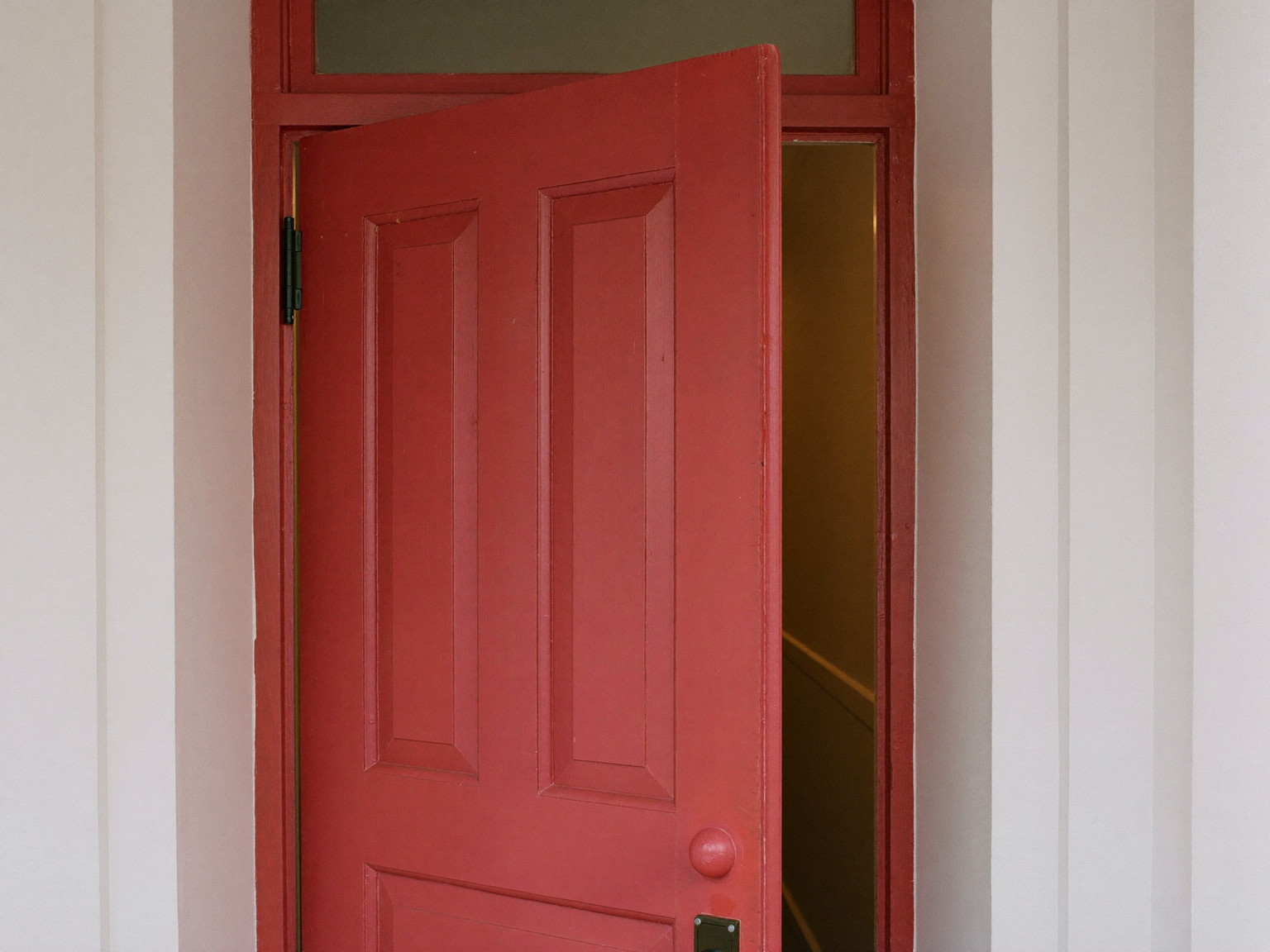 A traditional painted wooden front door standing slightly open in its freshly serviced frame inside a colonial entry: raised panels visible in barn-red