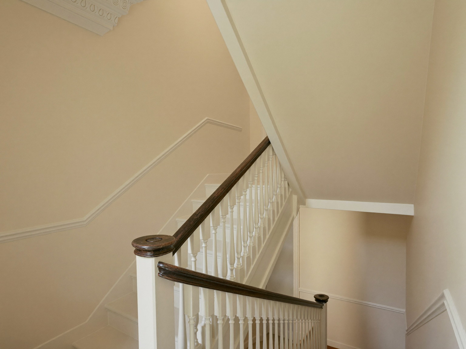 A finished repainted stair hall in a well-kept Millis colonial: soft cream walls over smooth restored plaster, bright white balusters with a refinished