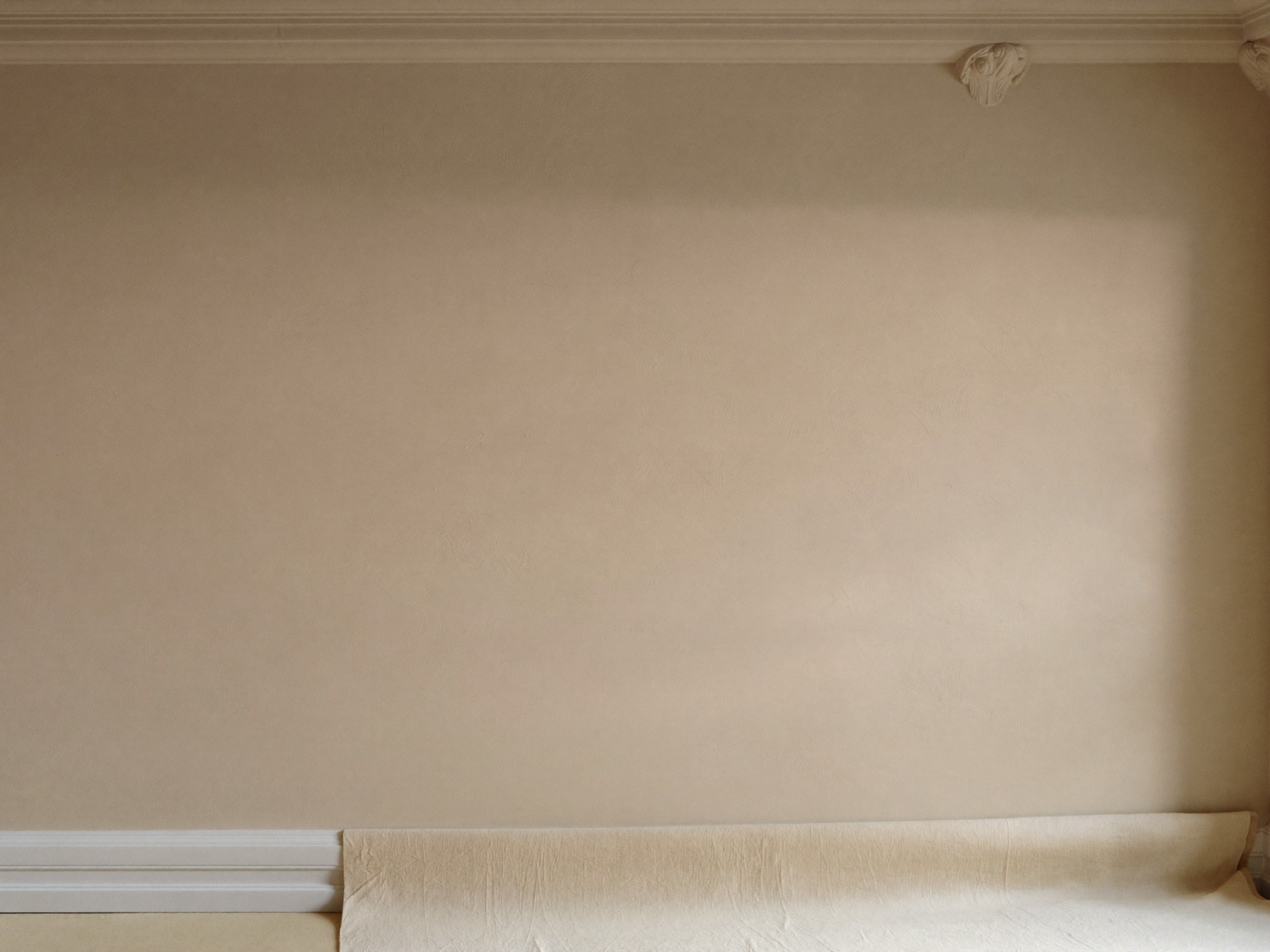 New skim-coat plaster drying under soft raking light in a well-kept colonial room, smooth flat even finish, tidy canvas drop cloth below, crisp white