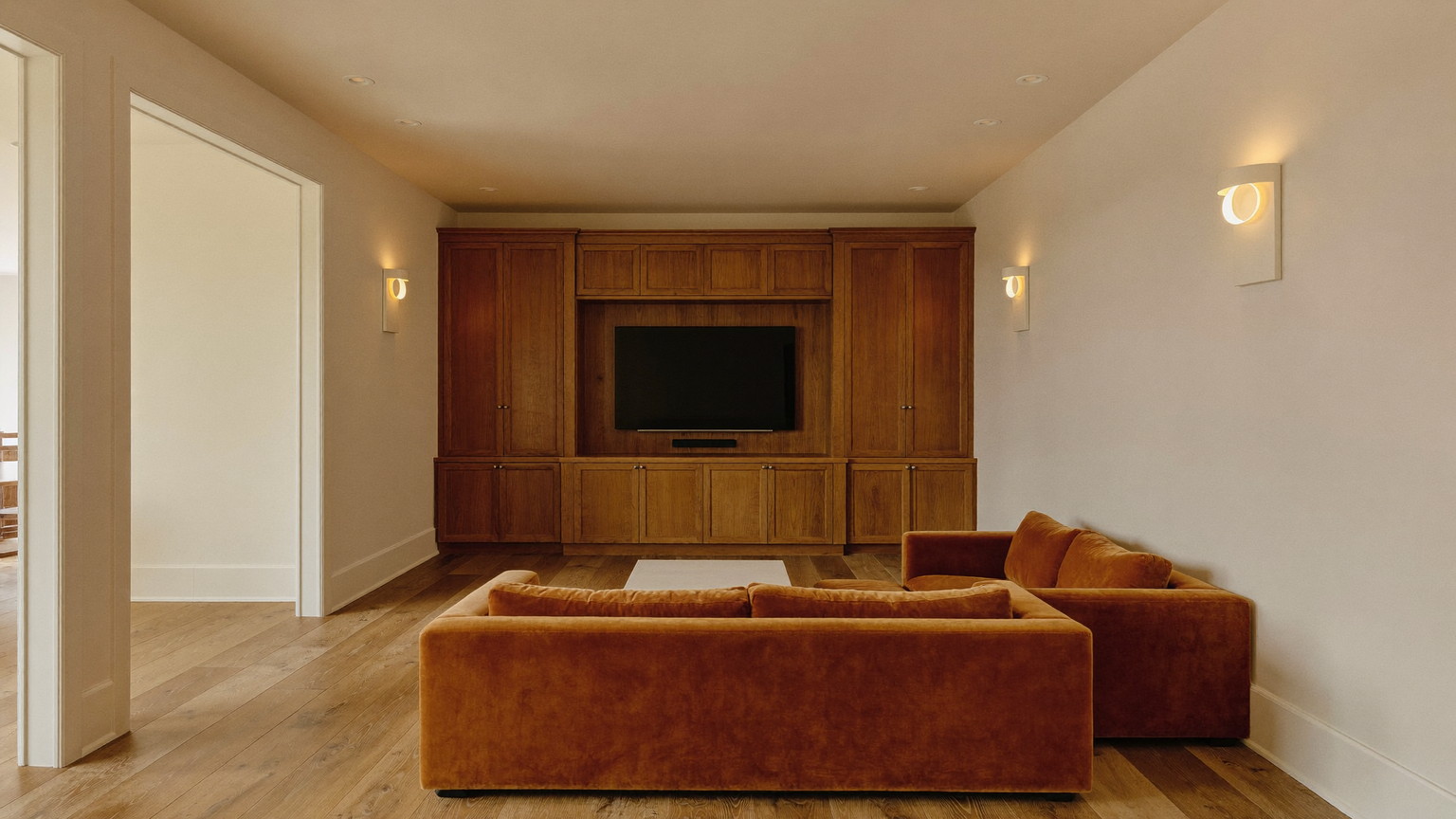 The finished lower level of an established Natick Massachusetts colonial, warm and lamplit: soft cream walls, cherry wood built-in media wall with plain