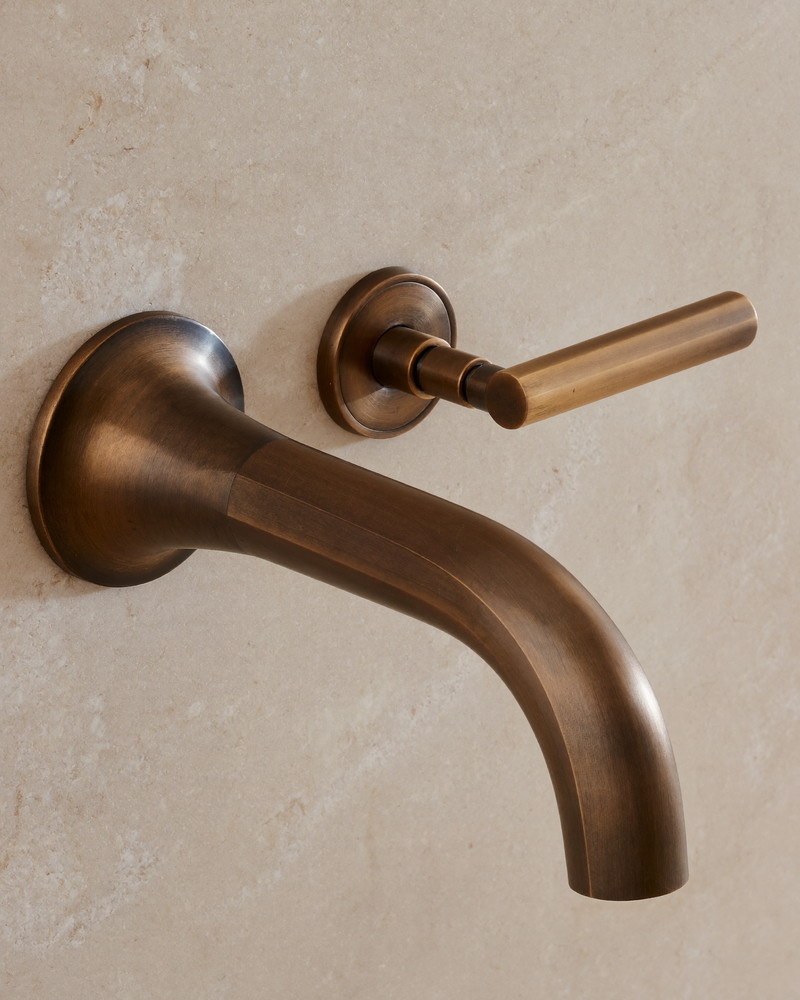 An aged bronze bathroom faucet with a smooth curved spout and lever handle mounted on pale quartzite, macro photograph from a slight angle, smooth