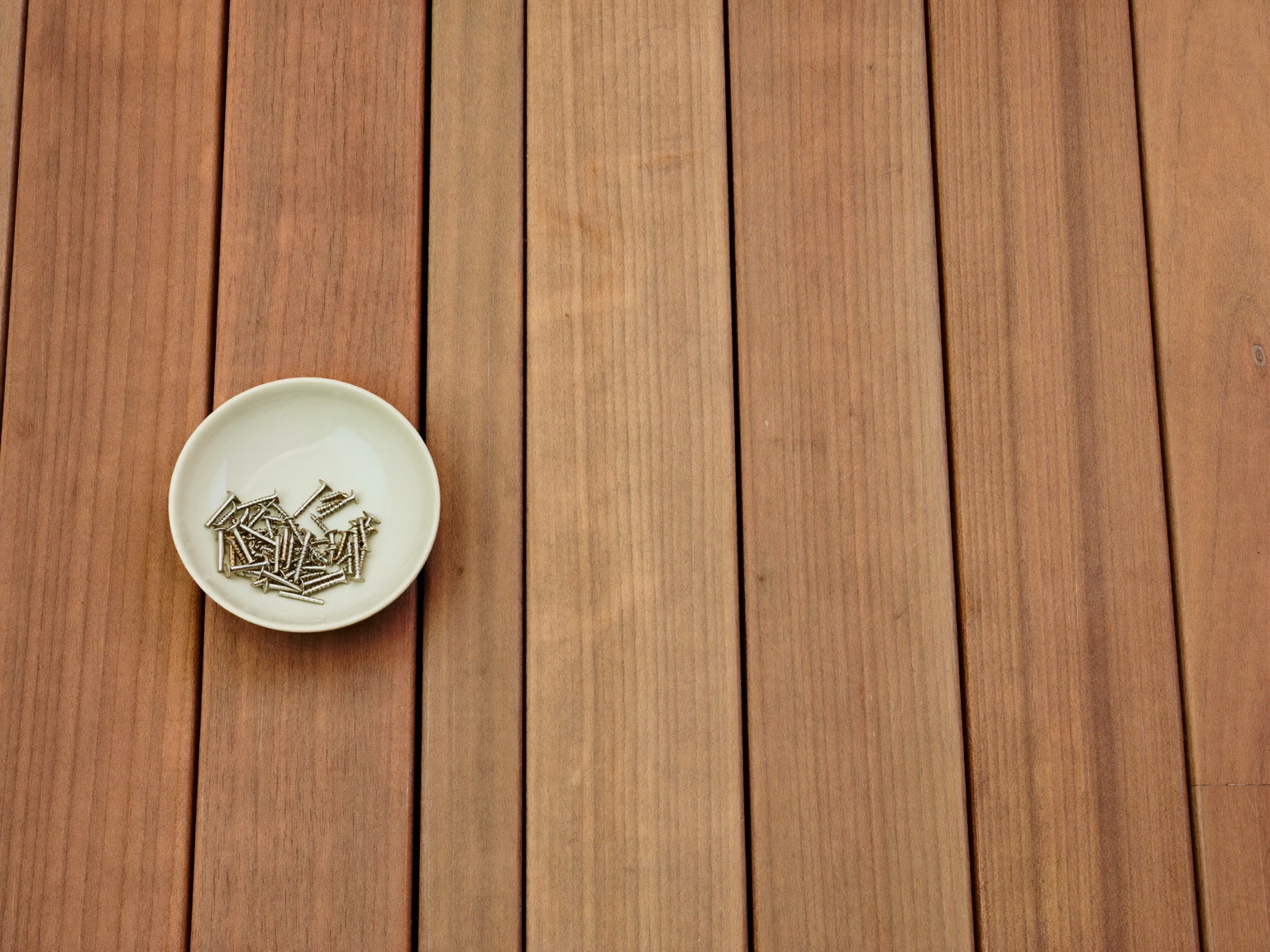 Overhead view of smooth new cedar deck boards laid side by side, every board surface completely blank bare and uniform in color, a small plain cream
