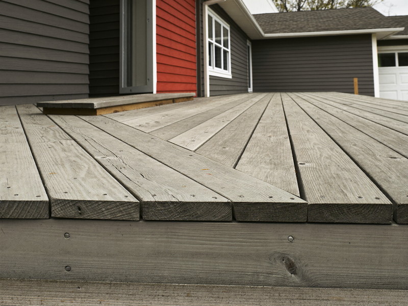 Close-up of an aged wooden deck board end on an established suburban home before repair: weathered gray surface, soft splintered grain at the cut end,