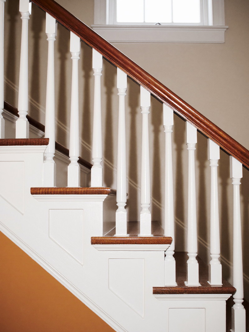 In an established colonial stairwell, a repaired balustrade: one new crisp white baluster fitted among originals beneath a refinished cherry handrail,