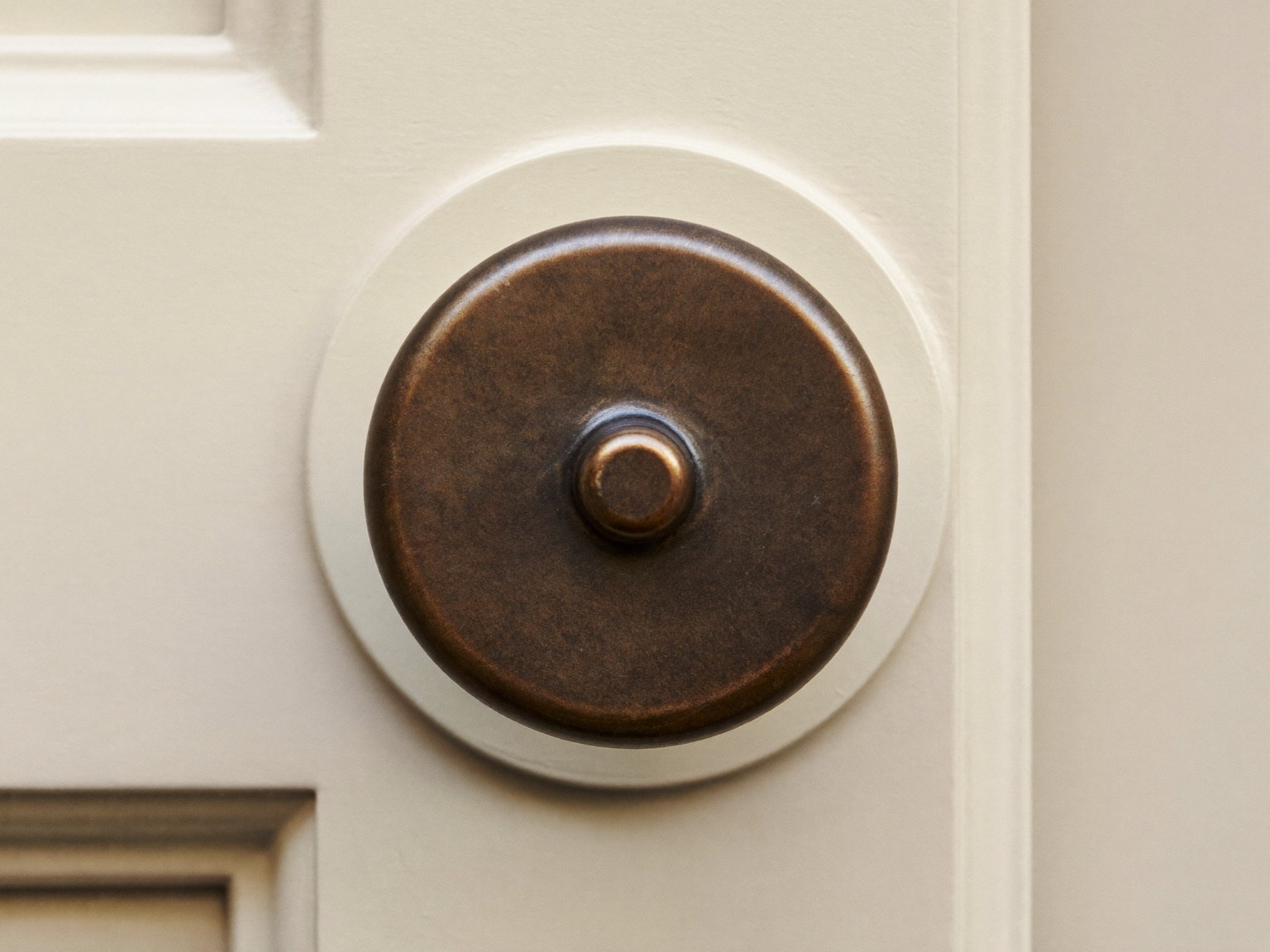 Macro photograph of an aged bronze round door knob with a perfectly plain smooth face on a simple round rosette, mounted on a cream paneled door, simple