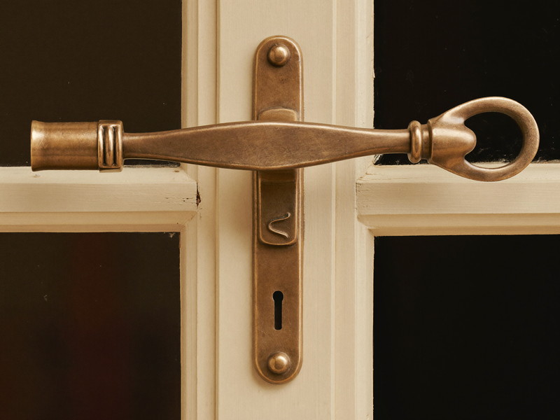Close view of a traditional aged bronze window sash lock with a curved swing arm where two cream painted wooden sashes meet, smooth plain metal, crisp