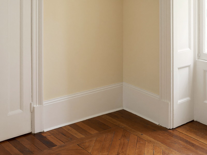 One restored corner of an established colonial room, where crisp white painted baseboard and white door casing meet a refinished warm cherry-toned wood
