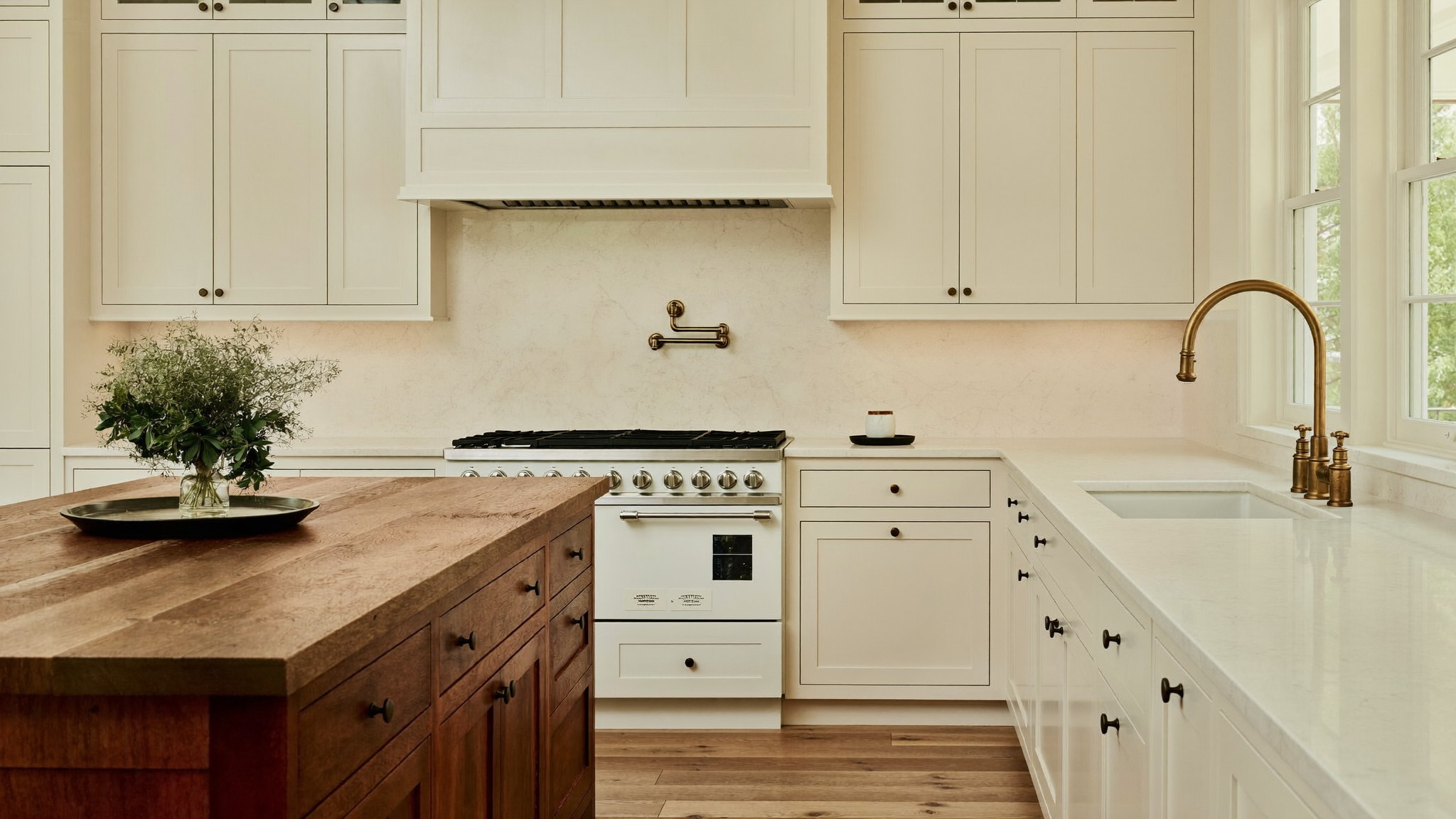 A renovated family kitchen inside an established Natick Massachusetts colonial, photographed editorially: warm white inset cabinetry, pale quartzite