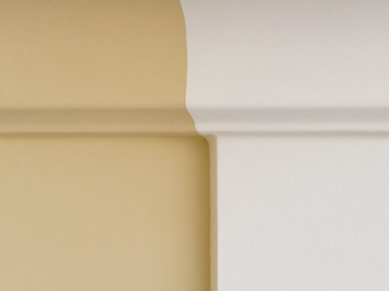 A razor-sharp masked paint line where a soft warm cream wall meets bright white crown molding, the edge perfectly straight and clean, smooth fresh paint
