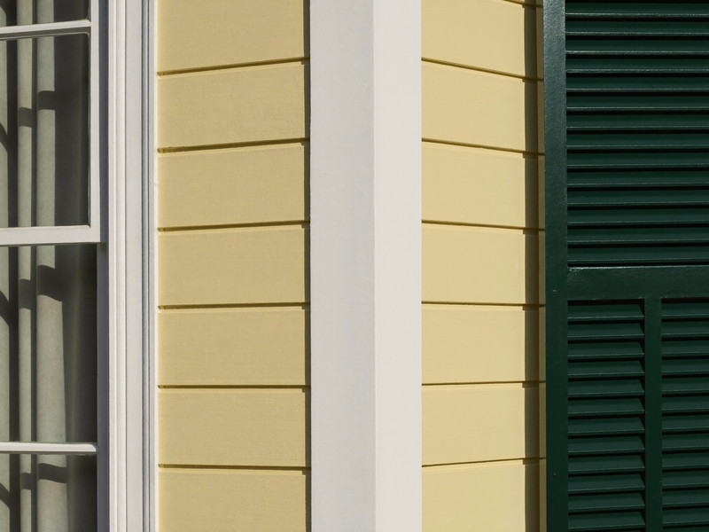 Detail of freshly repainted pale yellow clapboard siding on an established Natick colonial: narrow horizontal clapboards, a crisp white corner board, the